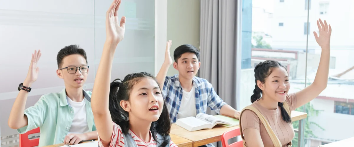 Students putting up their hand to volunteer to answer the teacher's question.
