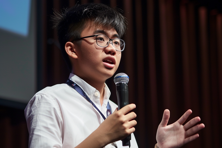 Male student confidently speaking into a microphone, demonstrating effective communication skills.