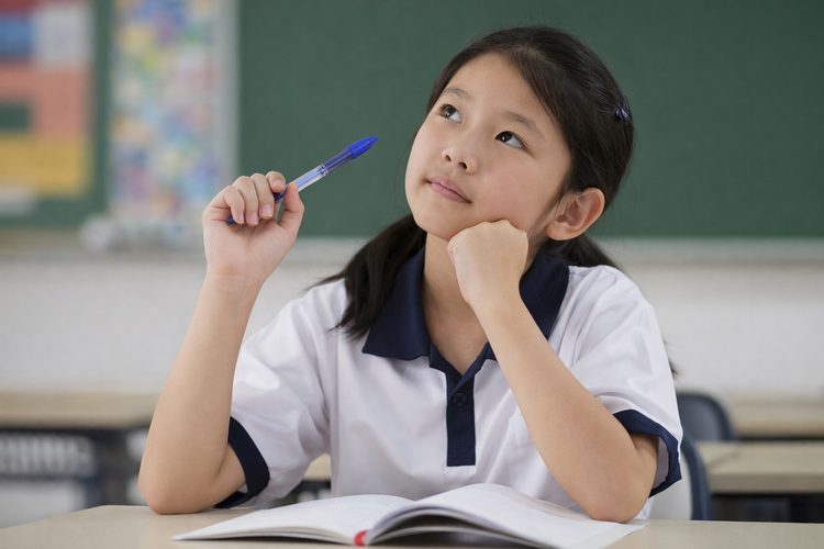 Primary school student thinking while holding a pen during an English exercise.