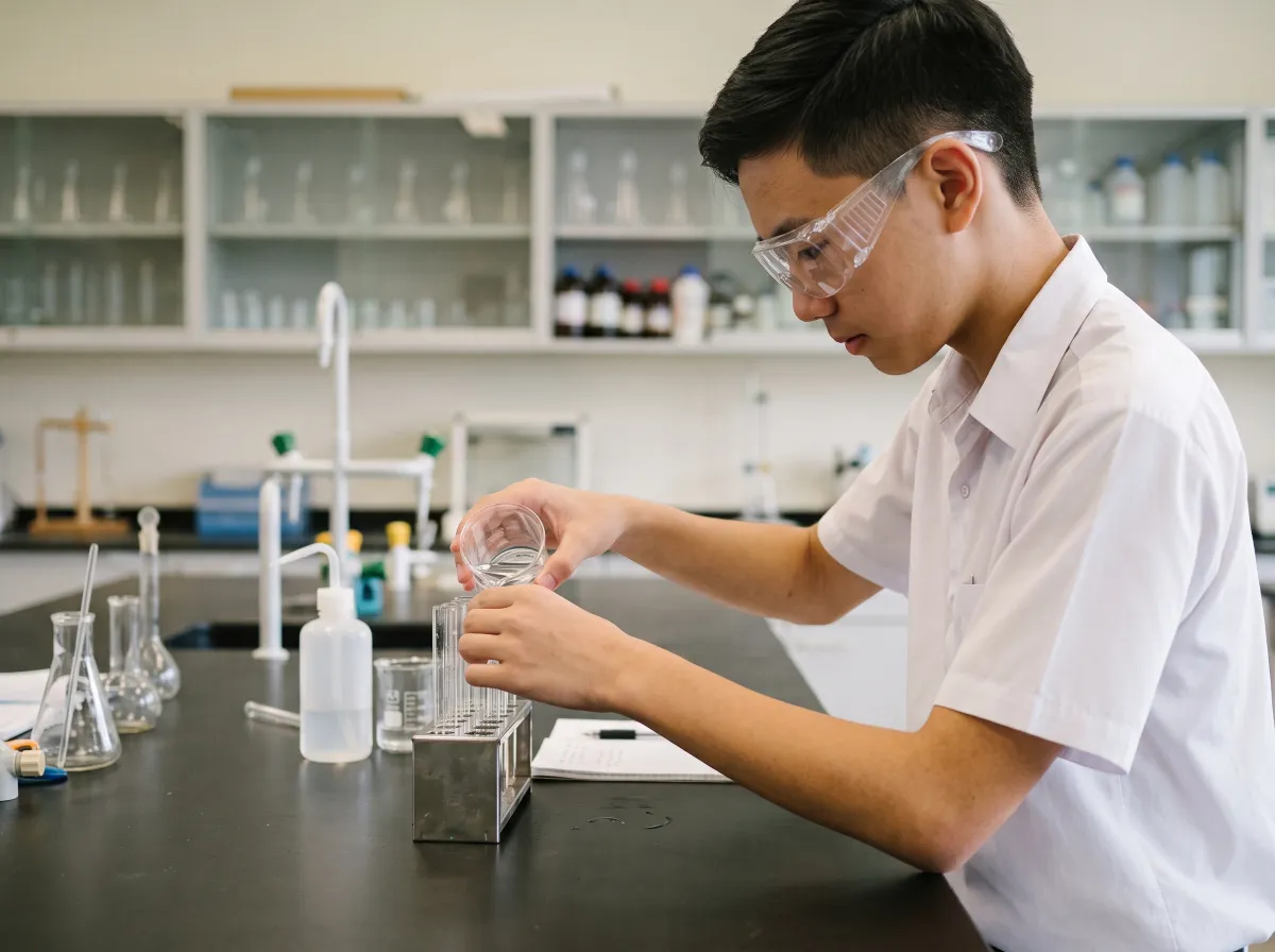 Student in goggles pouring liquid into a test tube in a junior college lab